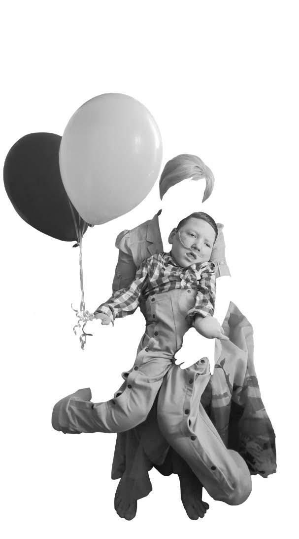 A woman sits holding a boy on her lap and balloons in her hand. Her face and arms are cut out of the picture so only her clothes and hair are visible