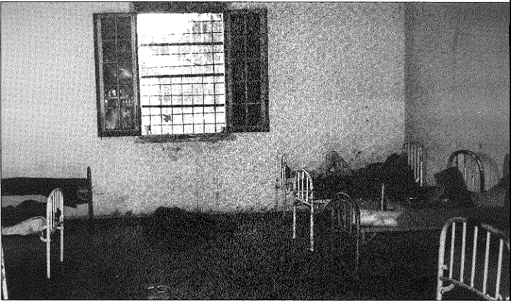 black and white photo of people lying in beds lined up against the walls in a bare room