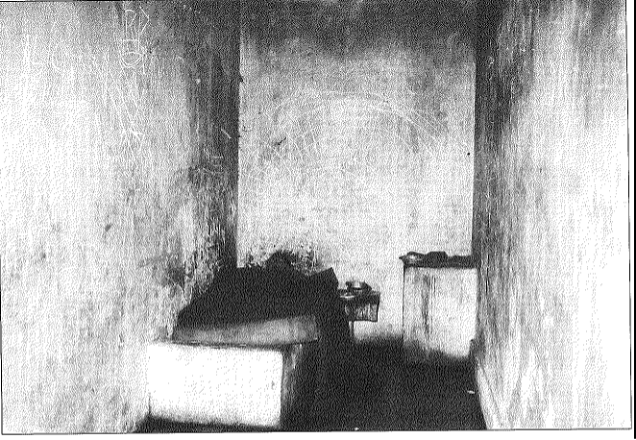 a person lying in a bed of a small bare room with no windows
