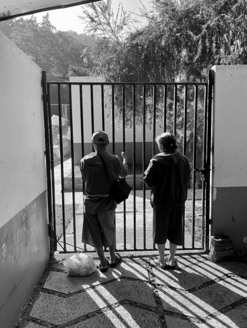 Two women stand with their backs to the camera holding on to bars of a gate