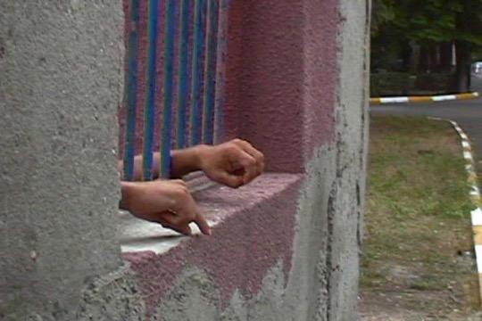 hands reaching through metal bars on a window of a concrete structure